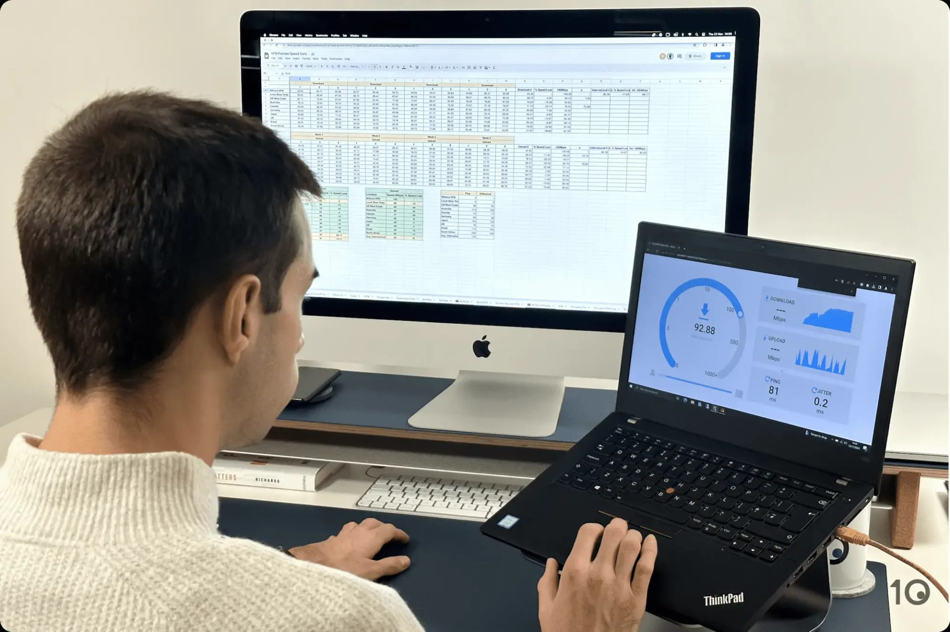 A man at a desk tests a VPN's speed performance on a laptop and analyzes a spreadsheet of speed test results on an iMac.